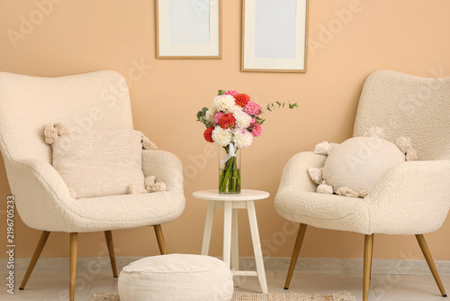 Table with bouquet of beautiful dahlia flowers and stylish armchairs near col...