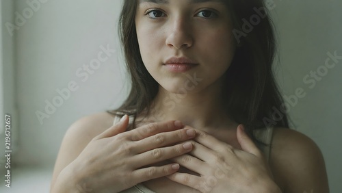 Description: Close-up portrait photography, ultra-sharp focus on facial expression and hands resting on chest. Natural skin tones, balanced exposure, zero facial distortion, clean depth of field. 