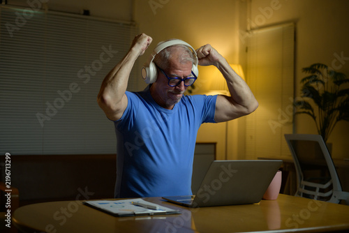 Senior man winning online game celebrating victory with headphones
