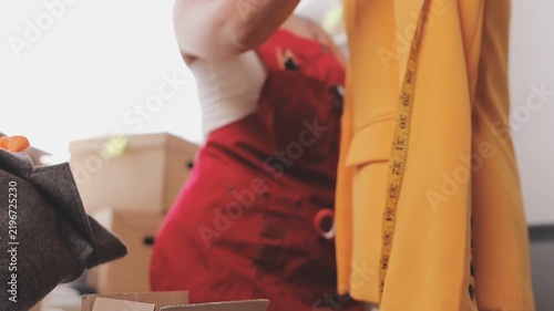 Confident Asian designer woman Beautiful smile using measuring tape for suit jacket with laptop computer in modern studio, clothes hanging on mannequin for customer online sales ordering.