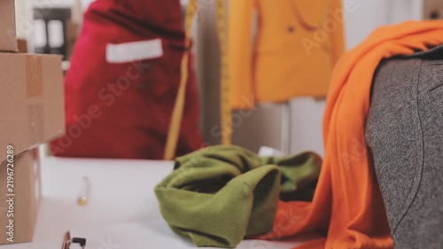 Confident Asian designer woman Beautiful smile using measuring tape for suit jacket with laptop computer in modern studio, clothes hanging on mannequin for customer online sales ordering.