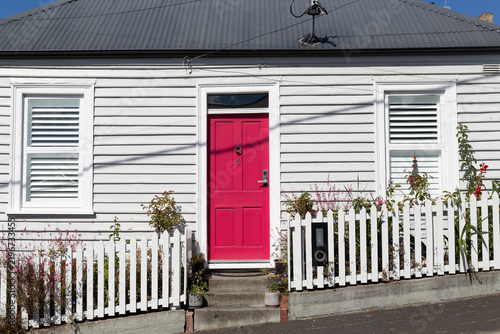 Weatherboard cottage painted grey with a bright red front door and a white picket fence