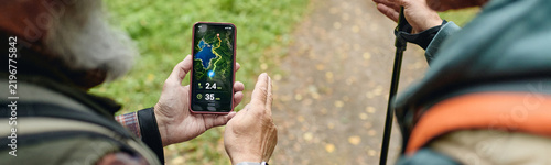Caucasian senior men holding smartphone with navigation app while trekking in forest. Concept of outdoor activity, retirement lifestyle, suitable for eco tourism and mobile tech promo