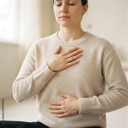 Photorealistic close-up photo of a person resting one hand on their chest and one hand on their abdomen while taking a slow breath, soft window light, pale neutral clothing and background, calm