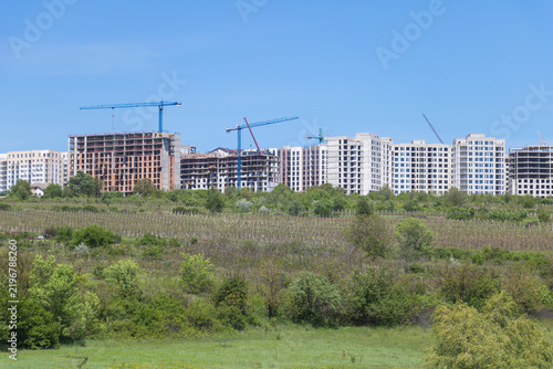 Fotografía Apartment buildings under construction with tower cranes rising beyond green agr