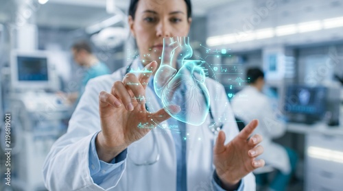 Female doctor examining glowing 3d hologram heart in high tech medical laboratory for cardiology and healthcare concept