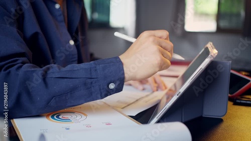 Businessman using a tablet and stylus pen with business performance reports placed on the desk.