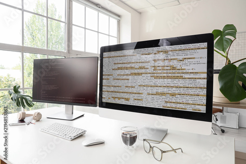 Software development and programming, computer monitors with code on a desk i...