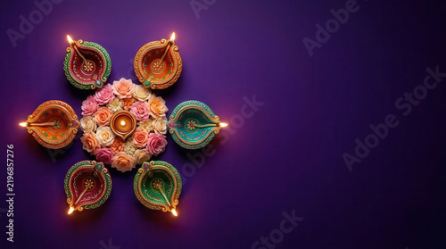 Flat lay of lit diya oil lamps arranged in circular mandala pattern with colorful flowers on purple background with copy space, festive traditional Indian Diwali festival of lights celebration
