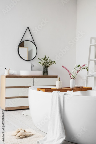 Interior of light bathroom with blooming branches in vases, sink and bathtub