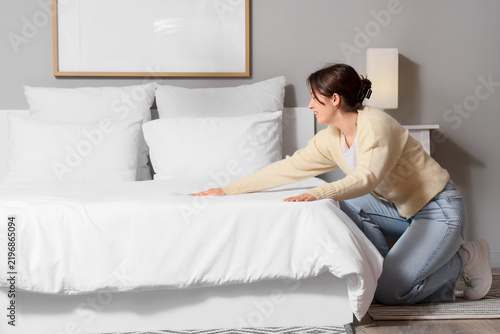 Beautiful young woman making bed in stylish bedroom