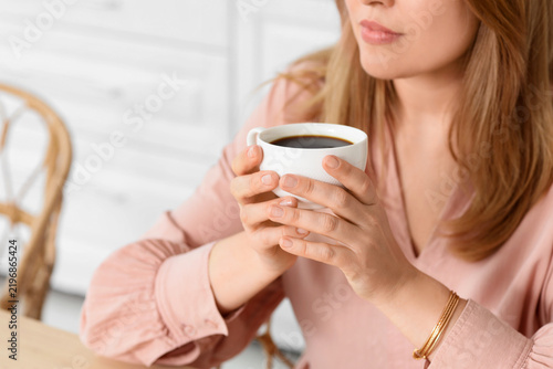 Beautiful woman with cup of coffee in kitchen, closeup