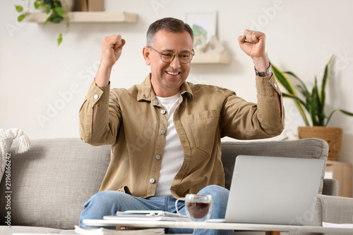 Success and achievement, happy mature man celebrating victory while working o...