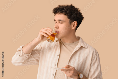 Young man drinking Turkish tea on beige background