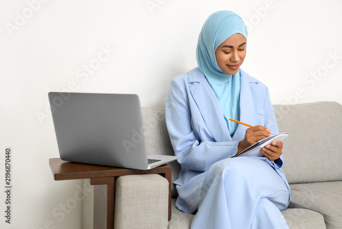 Young Muslim businesswoman learning Arabic language online on sofa in office