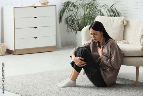 Young woman having panic attack on floor near sofa at home