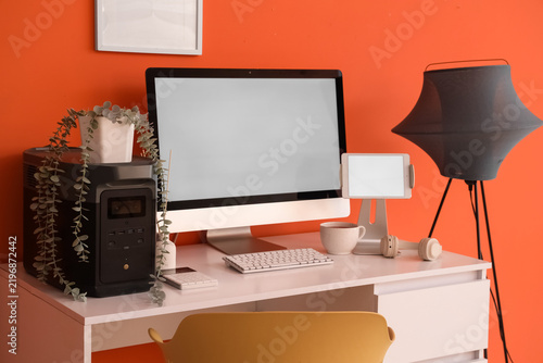 Inventors workplace with blank computer and lamp near orange wall in office