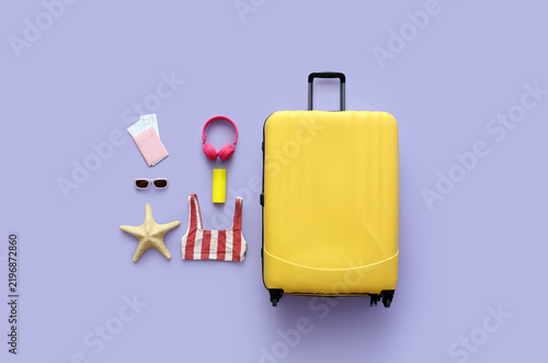 Suitcase, swimsuit and accessories on lilac background