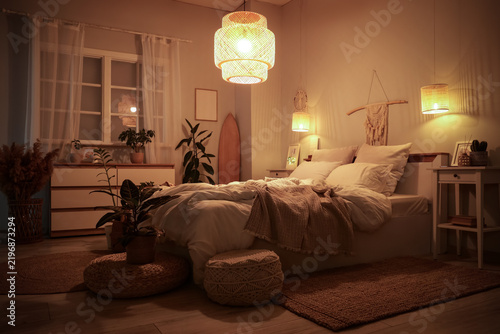 Interior of bedroom with surfboard, glowing lamps and plants at night
