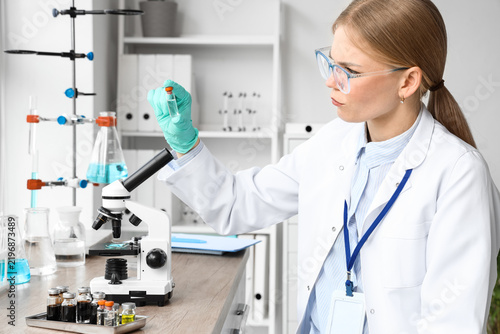 Female scientist with ampule and microscope working in laboratory