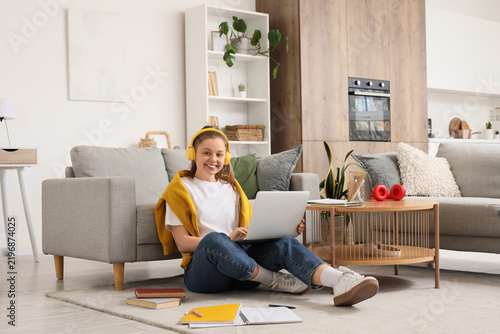 Teenage girl in headphones with laptop working online on floor at home