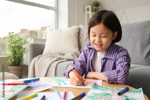 Cute Asian girl drawing on table at home