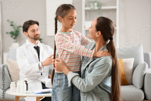 Cute girl hugging her mother against pediatrician at home