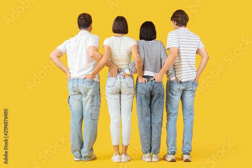 Group of young people in jeans on yellow background, back view
