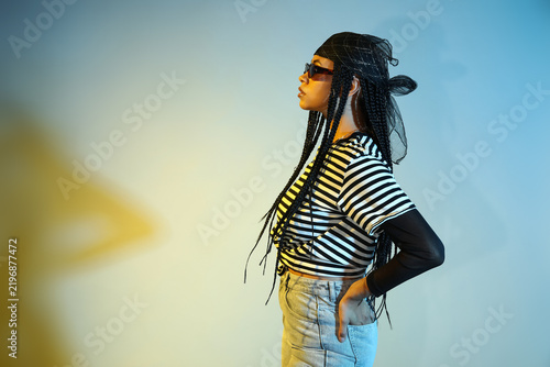 Cool young African-American woman with braids on color background