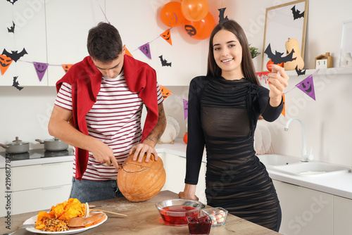 Young happy couple carving pumpkin in kitchen decorated for Halloween party