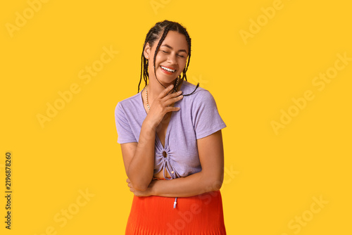 Beautiful young African-American woman with dreadlocks on yellow background