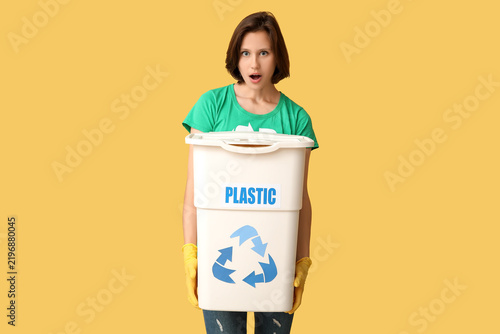 Fotografie Surprised female volunteer holding recycle bin for plastic garbage on yellow bac