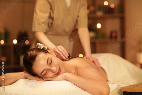 Beautiful woman getting massage with stones on couch in dark spa salon