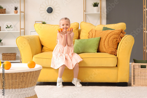 Cute little girl with orange pieces sitting on sofa at home
