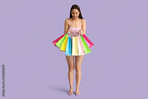 Beautiful young shocked woman in swimsuit with shopping bags on purple backgr...