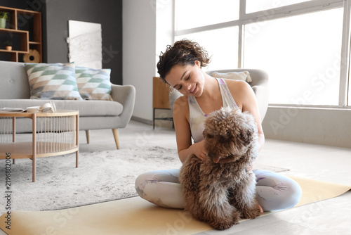 Sporty young woman with cute poodle sitting on mat at home