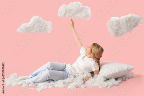 Adorable girl with white clouds lying on pink background