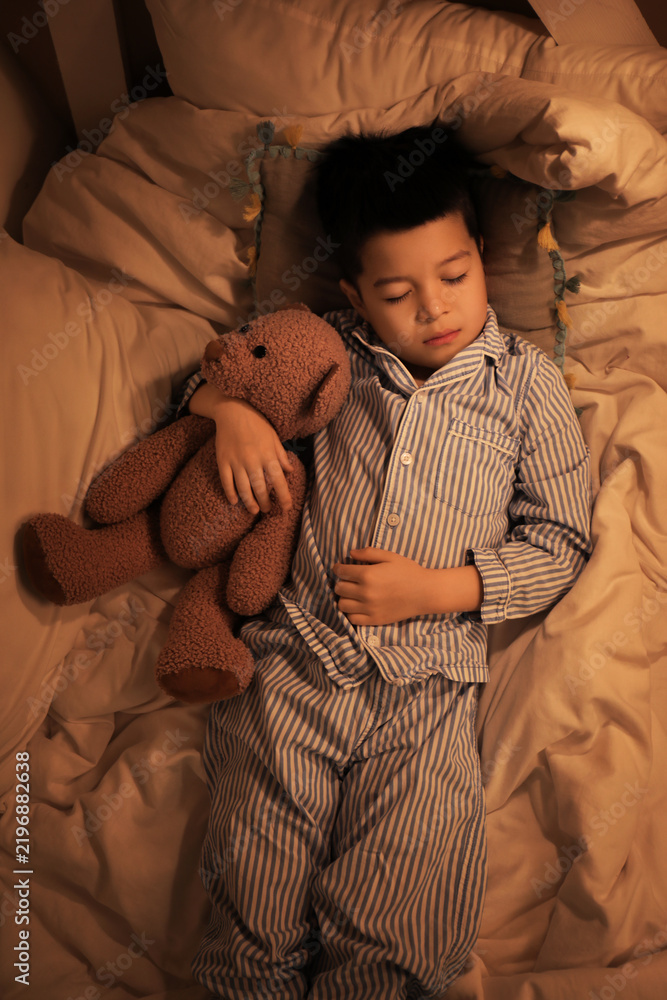 Obraz premium Cute little Asian boy in pajamas with toy bear sleeping in bed