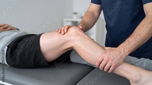 A physical therapist examining a patient's knee in a clinic setting.