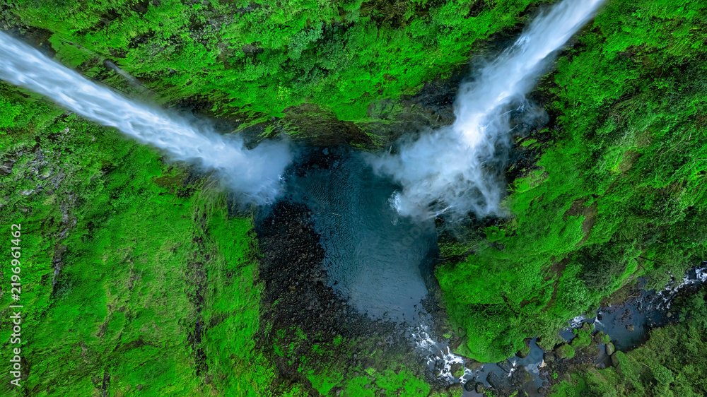 Obraz premium Aerial view of Tad Fane Waterfall in Laos, with a tourist enjoying tea while suspended on a zipline above the spectacular twin cascades and lush rainforest of the Bolaven Plateau.