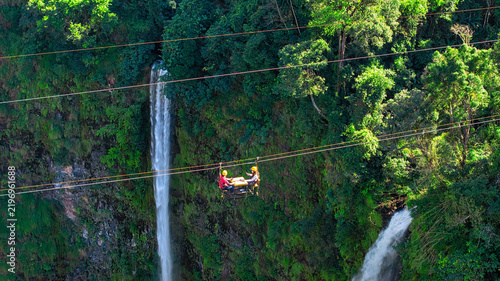 фотографія Aerial view of Tad Fane Waterfall in Laos, with a tourist enjoying tea while suspended on a zipline above the spectacular twin cascades and lush rainforest of the Bolaven Plateau