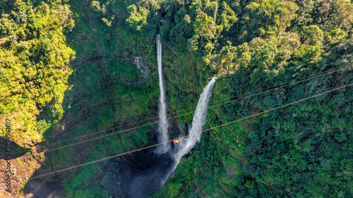 фотографія Aerial view of Tad Fane Waterfall in Laos, with a tourist enjoying tea while suspended on a zipline above the spectacular twin cascades and lush rainforest of the Bolaven Plateau