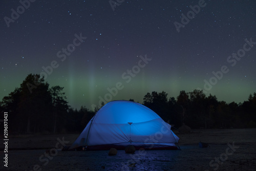 Glowing tent under a starry sky and northern lights