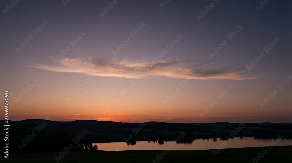 Fototapeta premium Serene Sunset Over a Calm Lake with Silhouetted Hills.