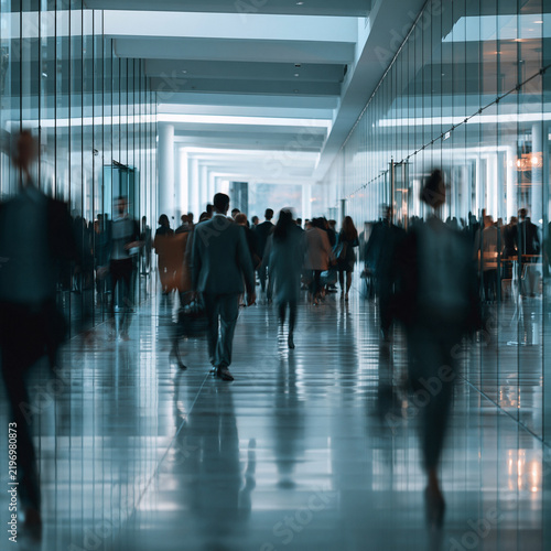 Blurred business people walking in a modern glass corporate corridor during rush hour. Perfect for urban commuter and corporate lifestyle concepts.