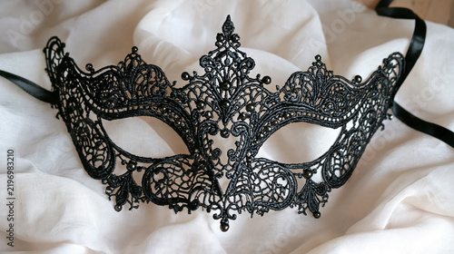 Elegant black lace masquerade mask resting on soft white silk fabric. This luxury accessory is perfect for gothic themes and glamorous Venetian carnival events.