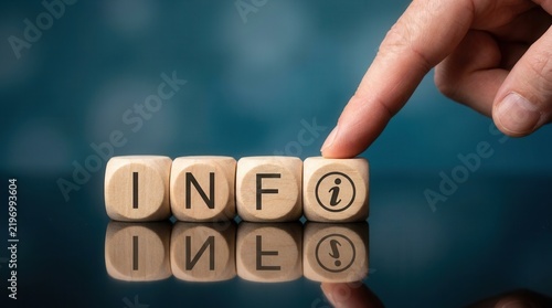 A hand touching a wooden block with an information symbol to complete the word INFO.