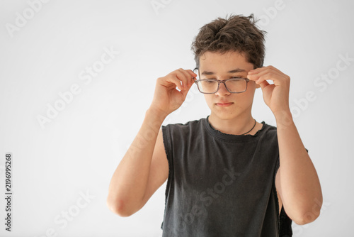 Cuadro en lienzo Teenage boy puts on glasses holding frame with both hands, eyesight worsening year after year, problem every second teenager has