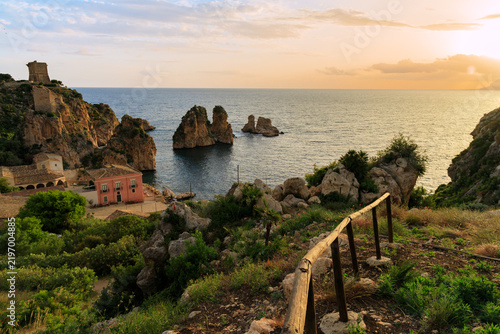 Scenic coastal landscape with a historic stone tower and villa at golden hour in Sicily