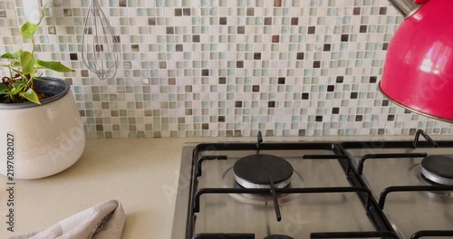 Lifting red kettle from gas stove. Modern domestic household kitchen appliances. Cozy morning routine beverage making.